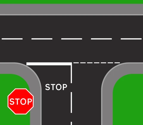 A stop junction from above. A solid white line runs across the mouth of the minor road with the word STOP painted on the road behind it, and an octagonal red STOP sign stands on the corner.