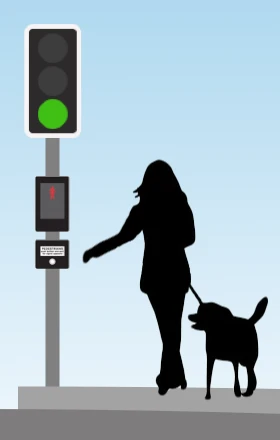 A pedestrian standing at a puffin crossing reaching for the push button. The control box carries a red standing figure on its face, and the traffic signal above shows green to traffic.